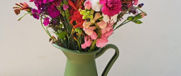 A 'Cornish Flowers - Mixed Bunch' from Mid July featuring Snapdragons, Cornflower, Crocosmia, Verbena, Alliums, Scented Pinks and Phlox - arranged in a green vase.