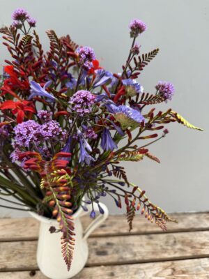 A close up of a jug of Agapanthus, Crocosmia & Verbena in a white tin jug.
