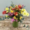 A mixed bouquet of Narcissi, Nerines and Chrysanthemums in a green tin jug