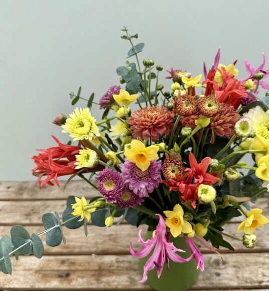 A mixed bouquet of Narcissi, Nerines and Chrysanthemums in a green tin jug